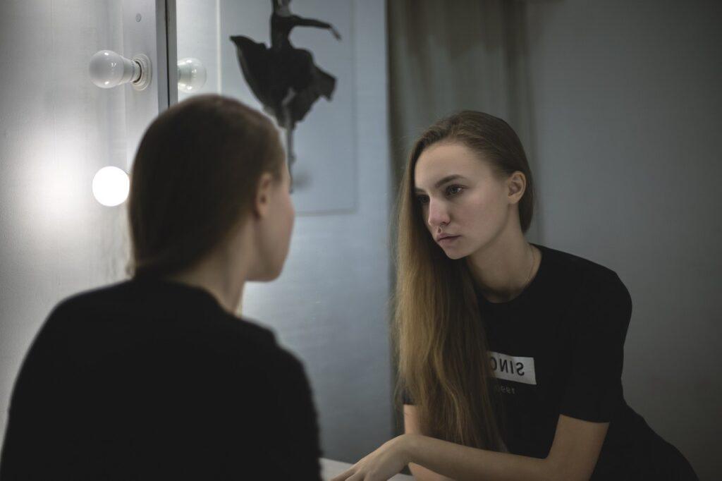 Woman looking in the mirror, facing her lack of self-awareness in relationships.