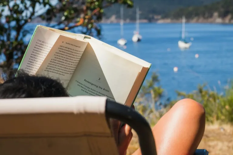 Woman reading a self improvement book on the beach, enjoying a relaxing summer day.