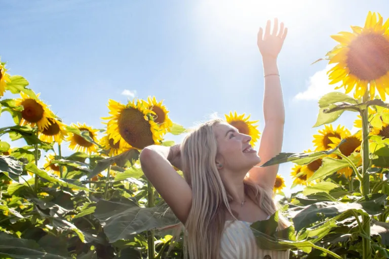 A happy woman in a sunflower field learned how to be happier in life every day.