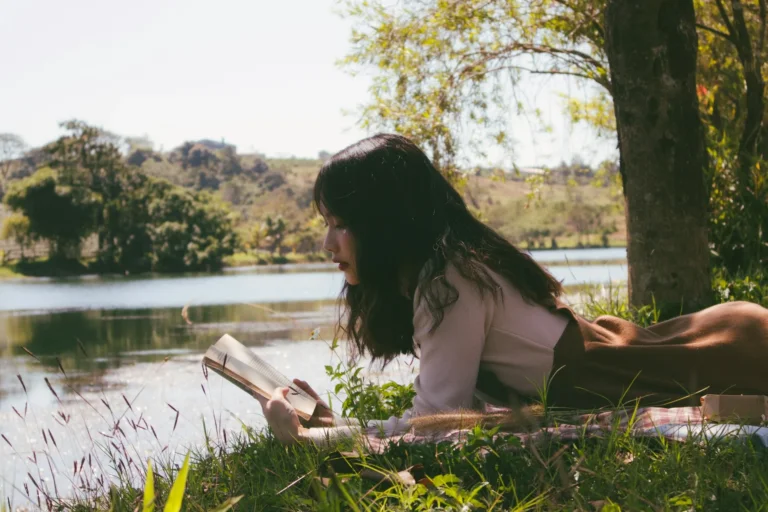 Woman sitting on the coast reading self help books for self love.
