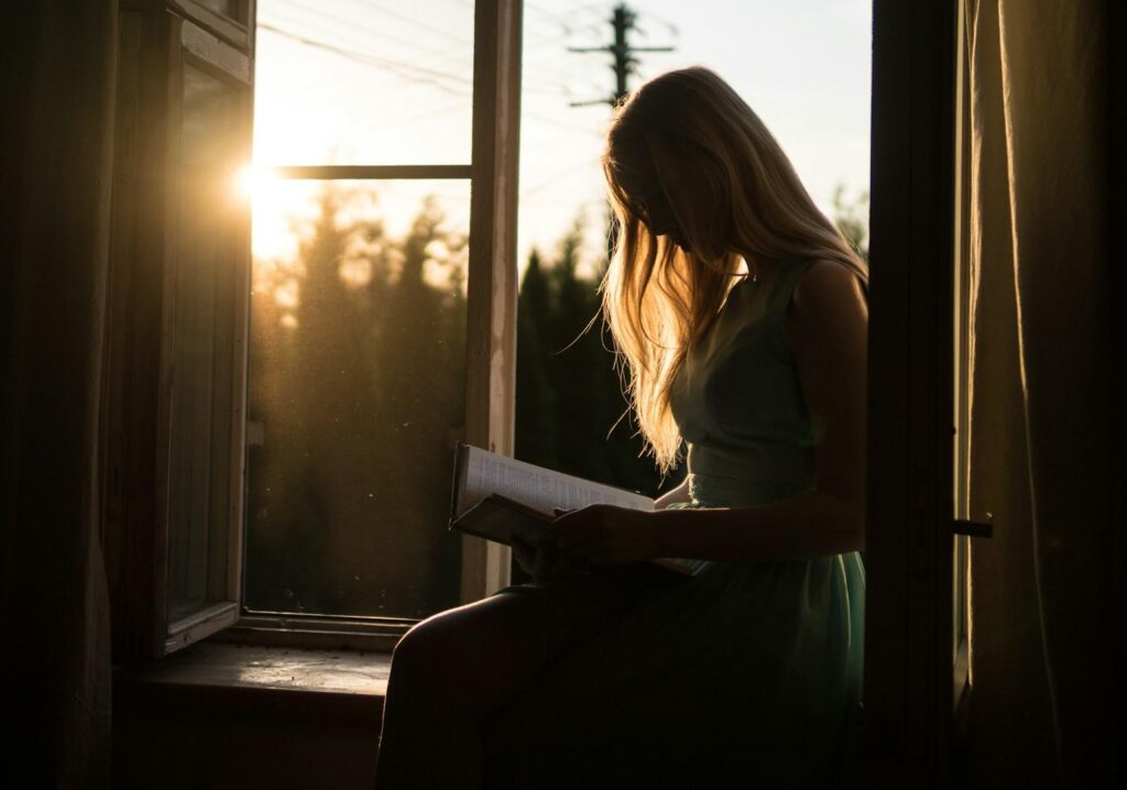 Woman reading on a window at sunset, reflecting on her healing journey.