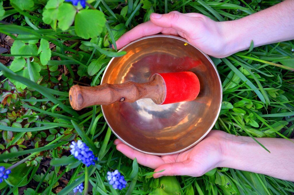 Person holding a singing bowl in grass, preparing for a sound therapy session.