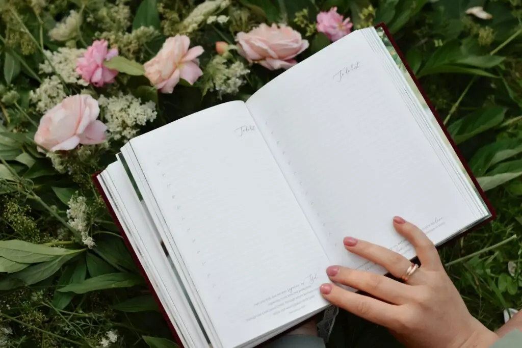 A hand holding an open journal in front of flowers, representing growth that comes from journaling for self esteem.