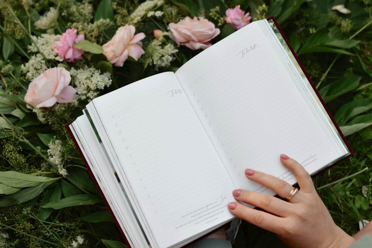 A hand holding an open journal in front of flowers, representing personal growth.