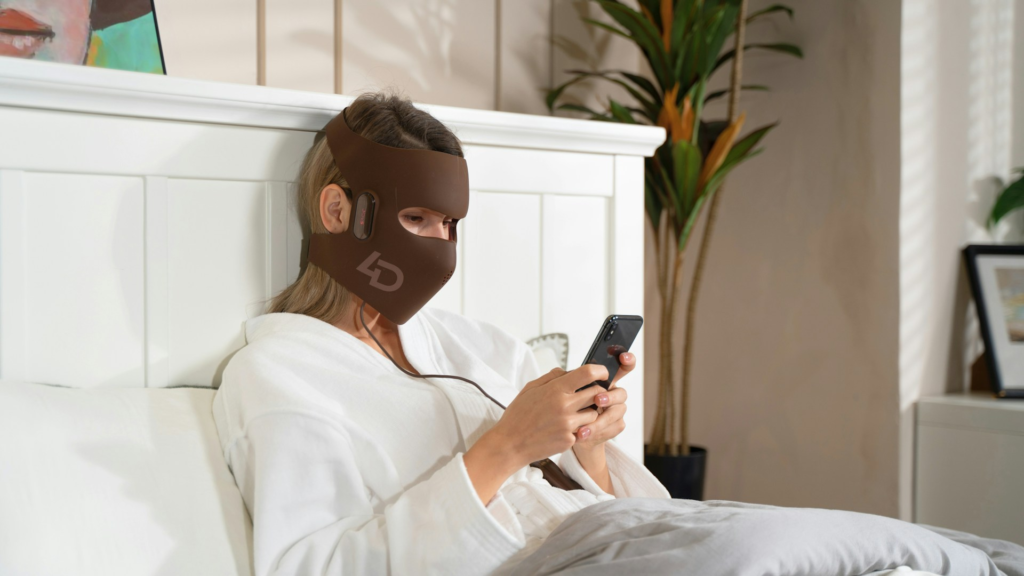 Woman wearing a red light therapy mask as one of the ways to glow up at home.