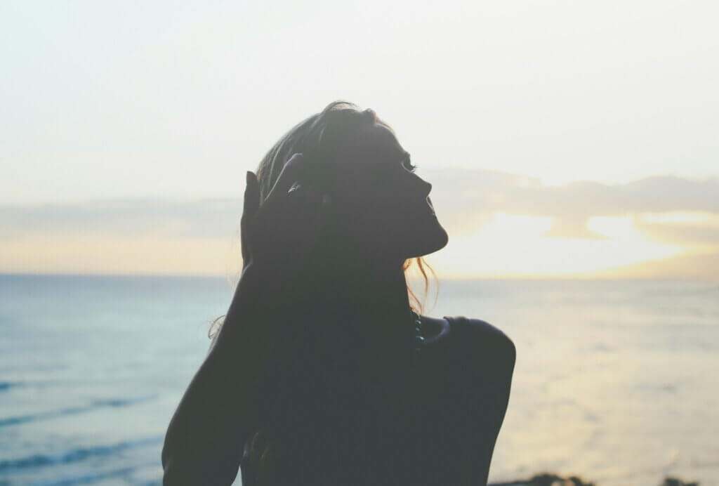 Silhouette of a woman on a beach, reflecting on herself after journaling for self-esteem.