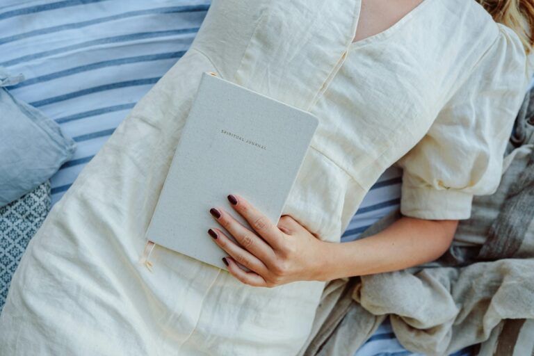 Woman laying on the best with her manifestation journal, representing how to manifest faster without forcing manifestation.