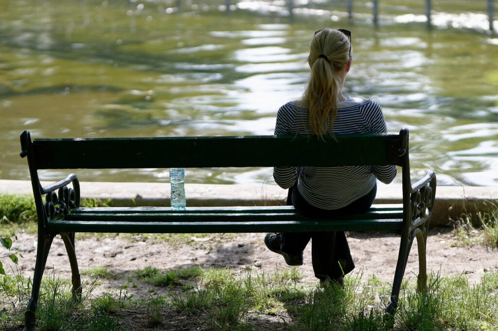 Woman sitting on a bench near water, thinking of why manifesting love feels so hard right now.