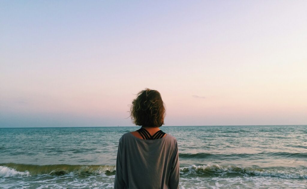 Woman by the ocean, reflecting on her daily gratitude practice.