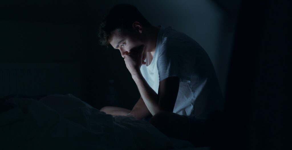Man having disrupted sleep because of phone addiction.
