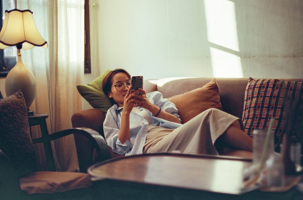 Woman scrolling on her phone while lying on a couch.